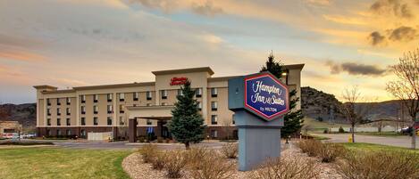 A Hampton Inn & Suites by Hilton building with a sign, surrounded by a landscaped area with a tree and gravel path.