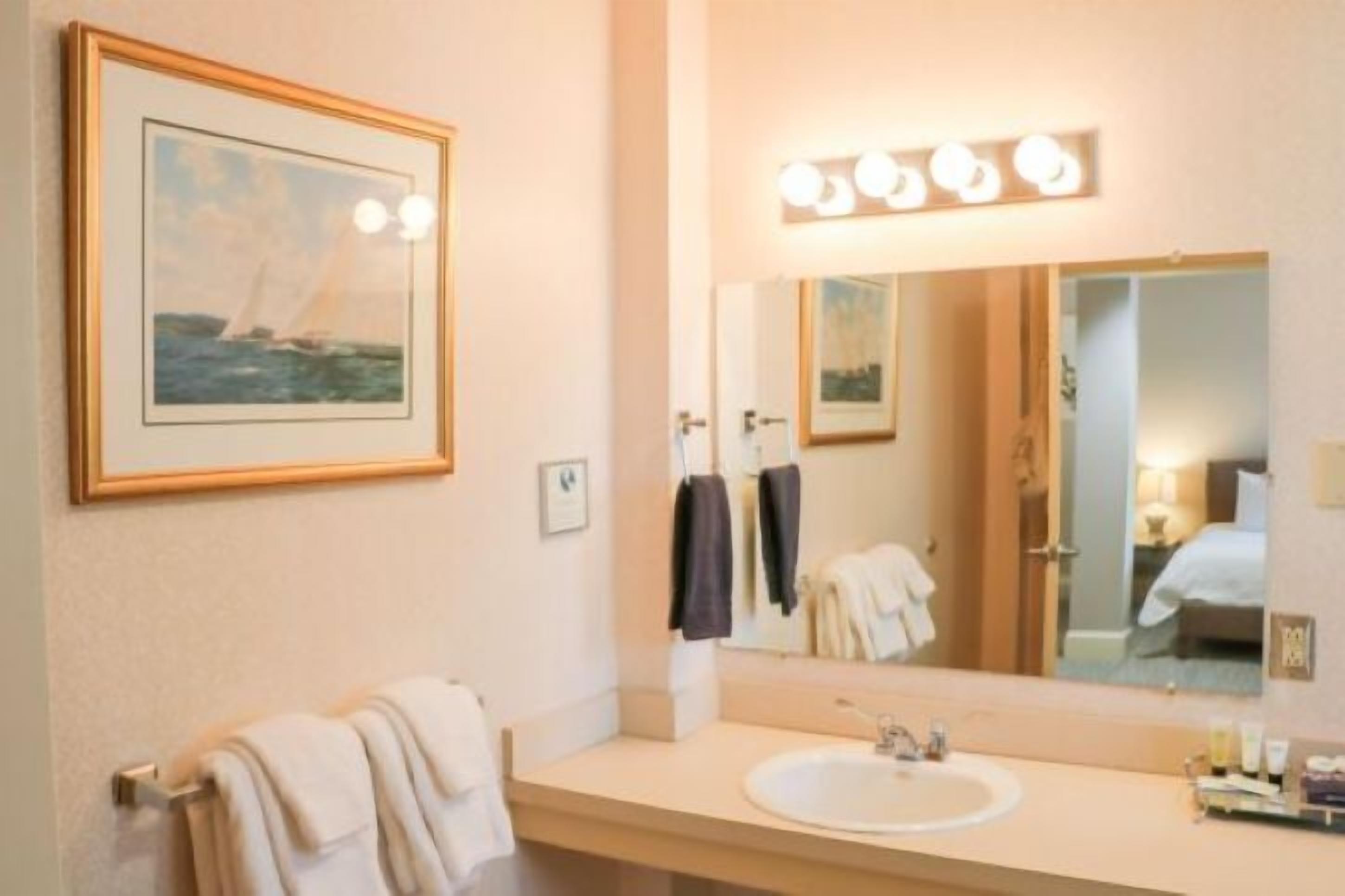 A hotel bathroom with a large mirror, a sink, and a framed picture of a sailboat on the wall.