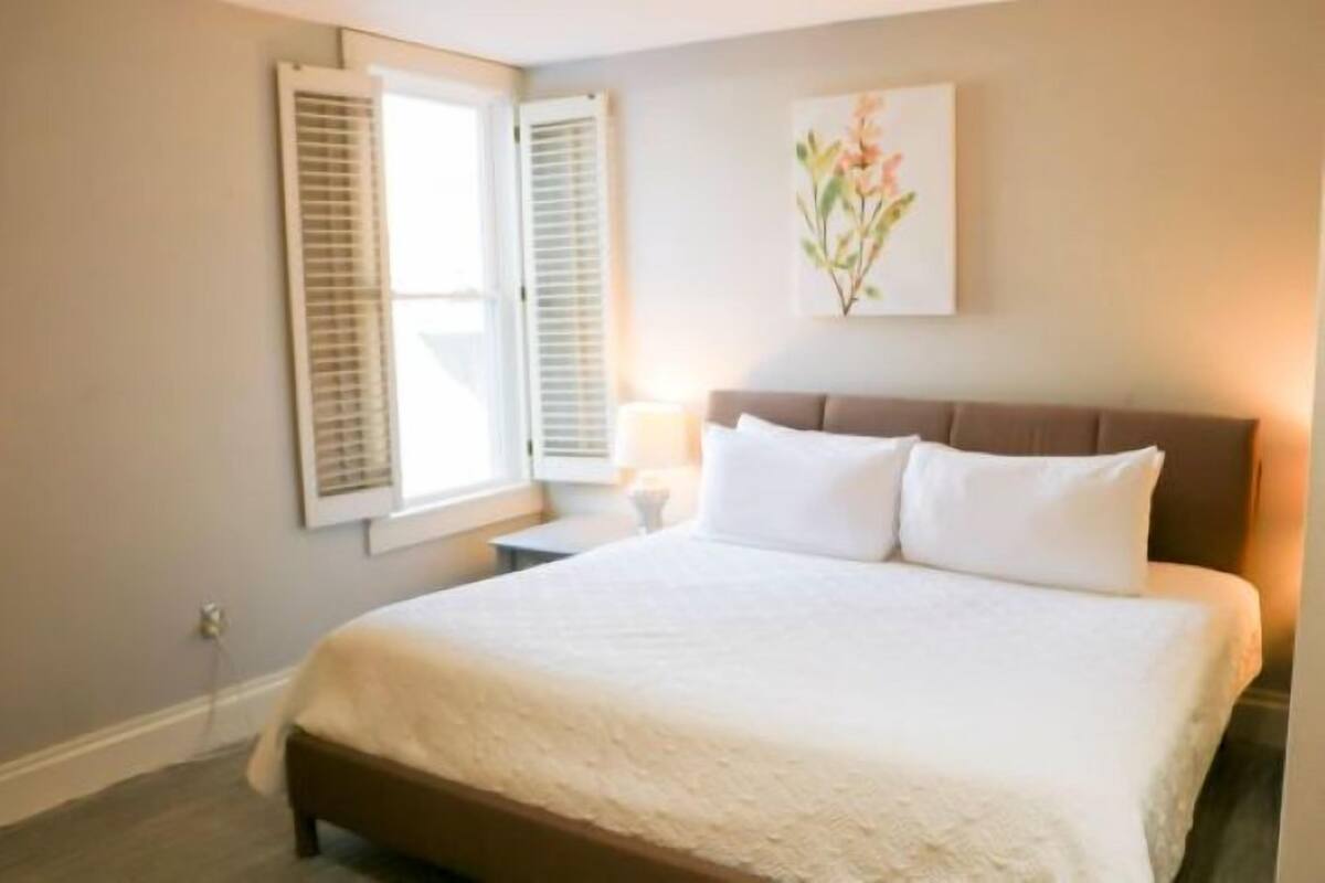 A bedroom with a large bed, a nightstand, a lamp, and a window with shutters.