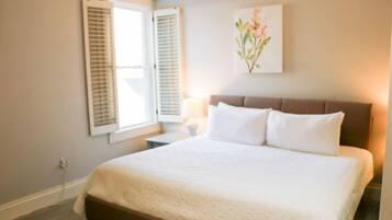 Un dormitorio con una cama grande, una mesita de noche, una lámpara y una ventana con contraventanas.