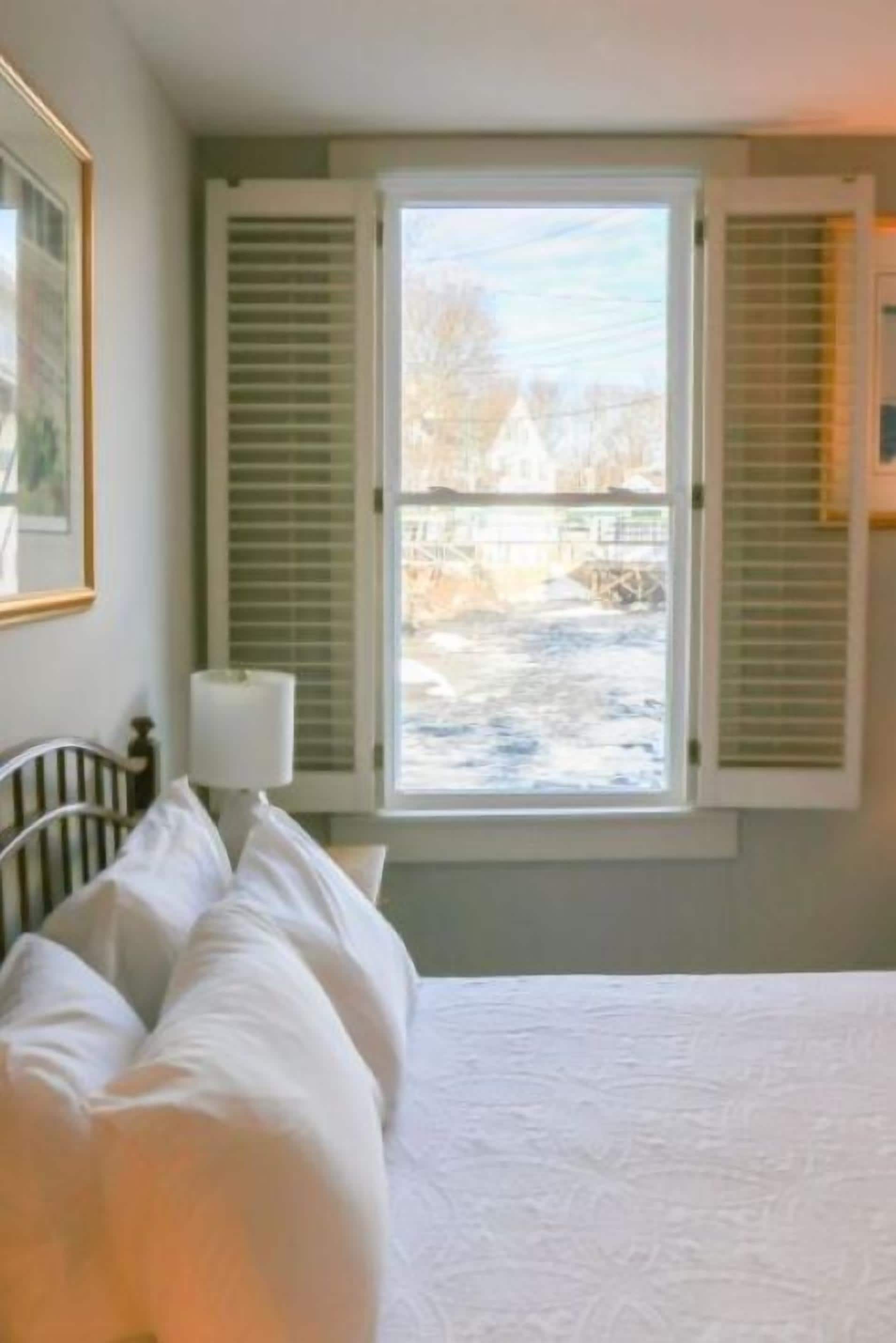 A bedroom with a bed, a window with blinds, a lamp, and a framed picture on the wall.