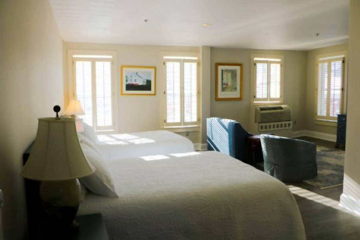 A hotel room with a large bed, a desk, a chair, and two windows.