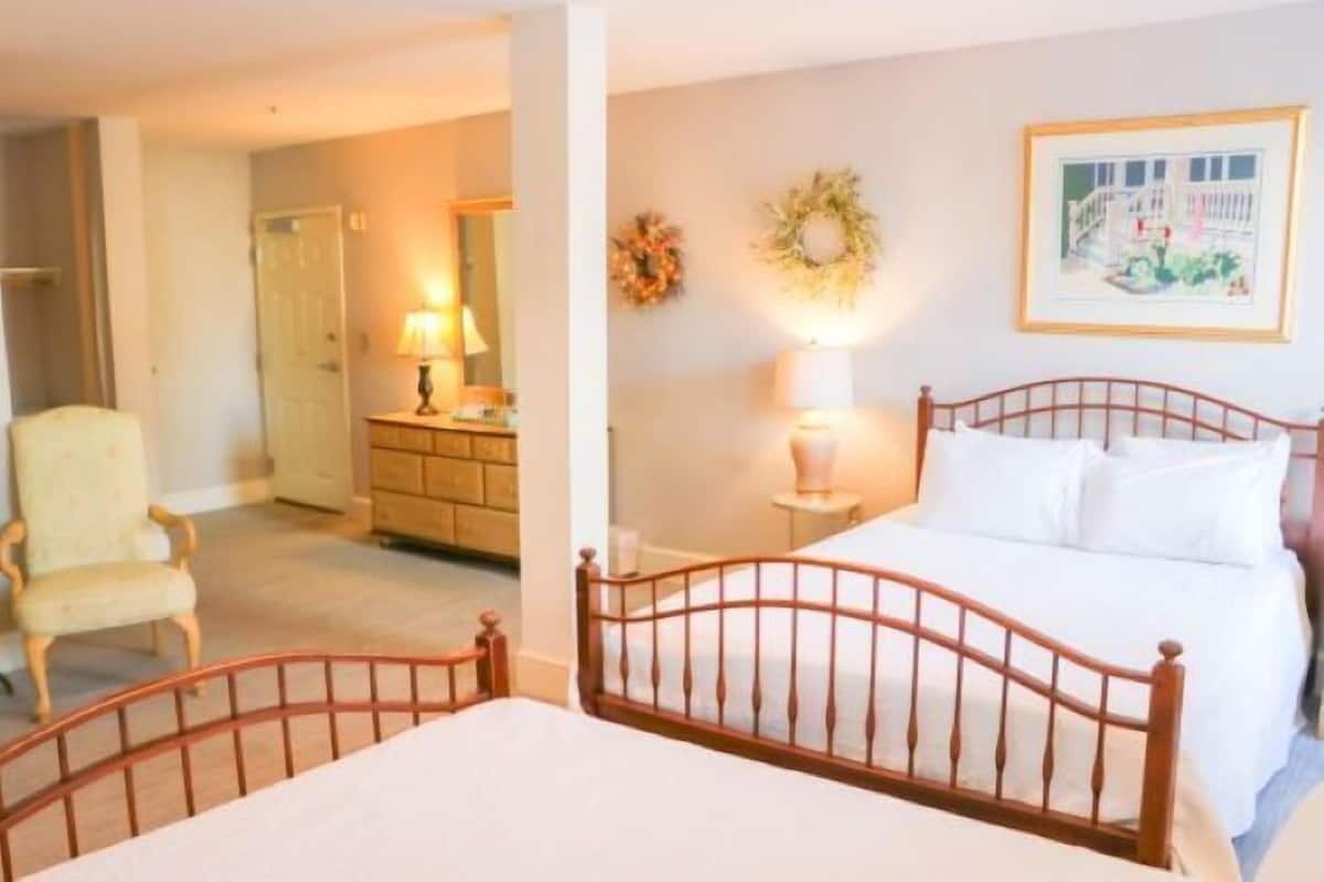 A bedroom with a wooden bed, a chair, a dresser, and a wall with a framed picture and two wreaths.