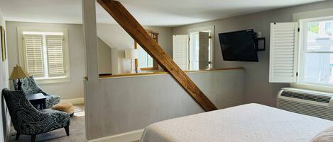 A bedroom with a large bed, a chair, a desk, a TV, and a window with shutters.