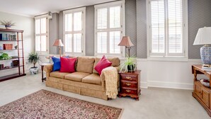 Een woonkamer met een beige bank, een kamerbreed tapijt met dessin, een houten bijzettafeltje en een boekenkast.