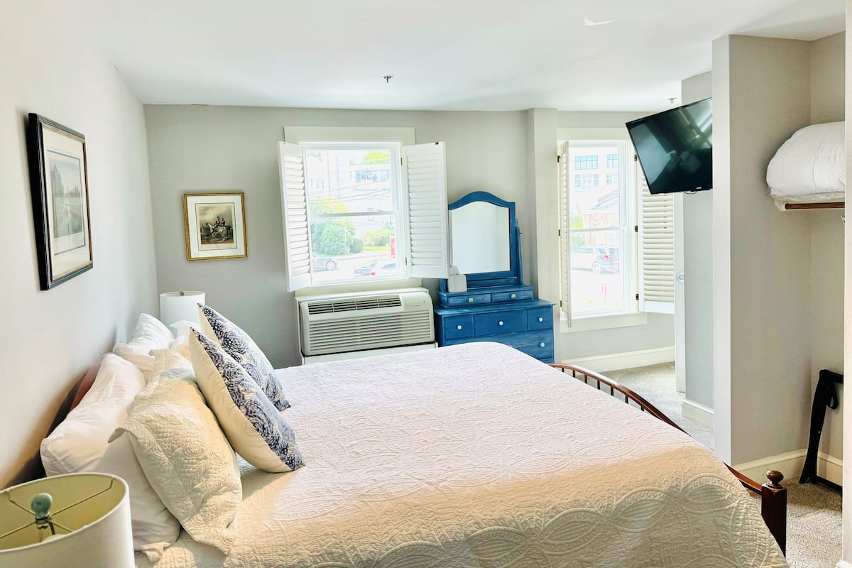 A bedroom with a bed, a dresser, a television, and a window with blinds.