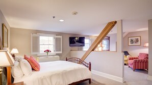 Een slaapkamer met een houten bed, een aan de muur bevestigde televisie en een trap naar een andere kamer.
