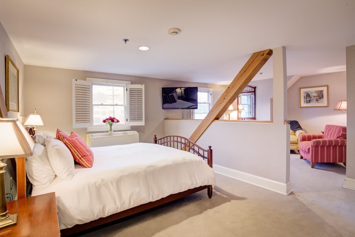 A bedroom with a wooden bed, a television mounted on the wall, and a staircase leading to another room.