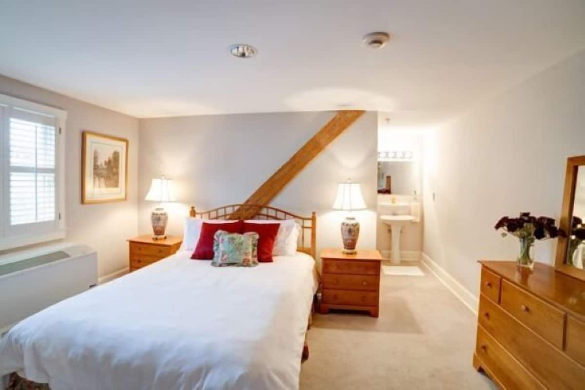 A bedroom with a bed, two bedside tables with lamps, a dresser, a mirror, and a window with blinds.
