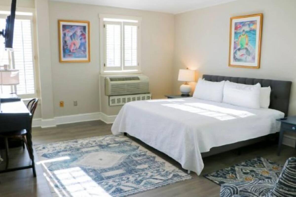 A bedroom with a bed, a desk, a chair, a lamp, and two paintings on the wall.