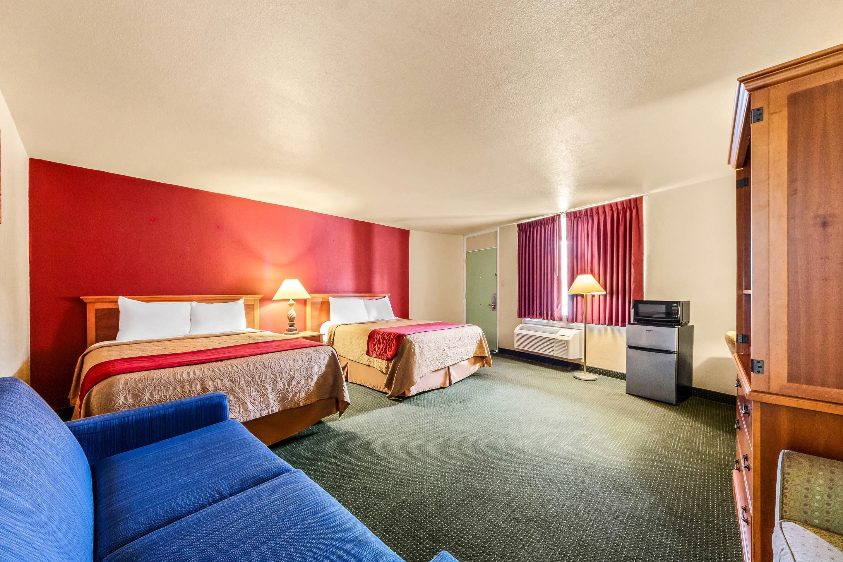 Une chambre d’hôtel avec deux lits, un canapé, un bureau avec un ordinateur et un four à micro-ondes.