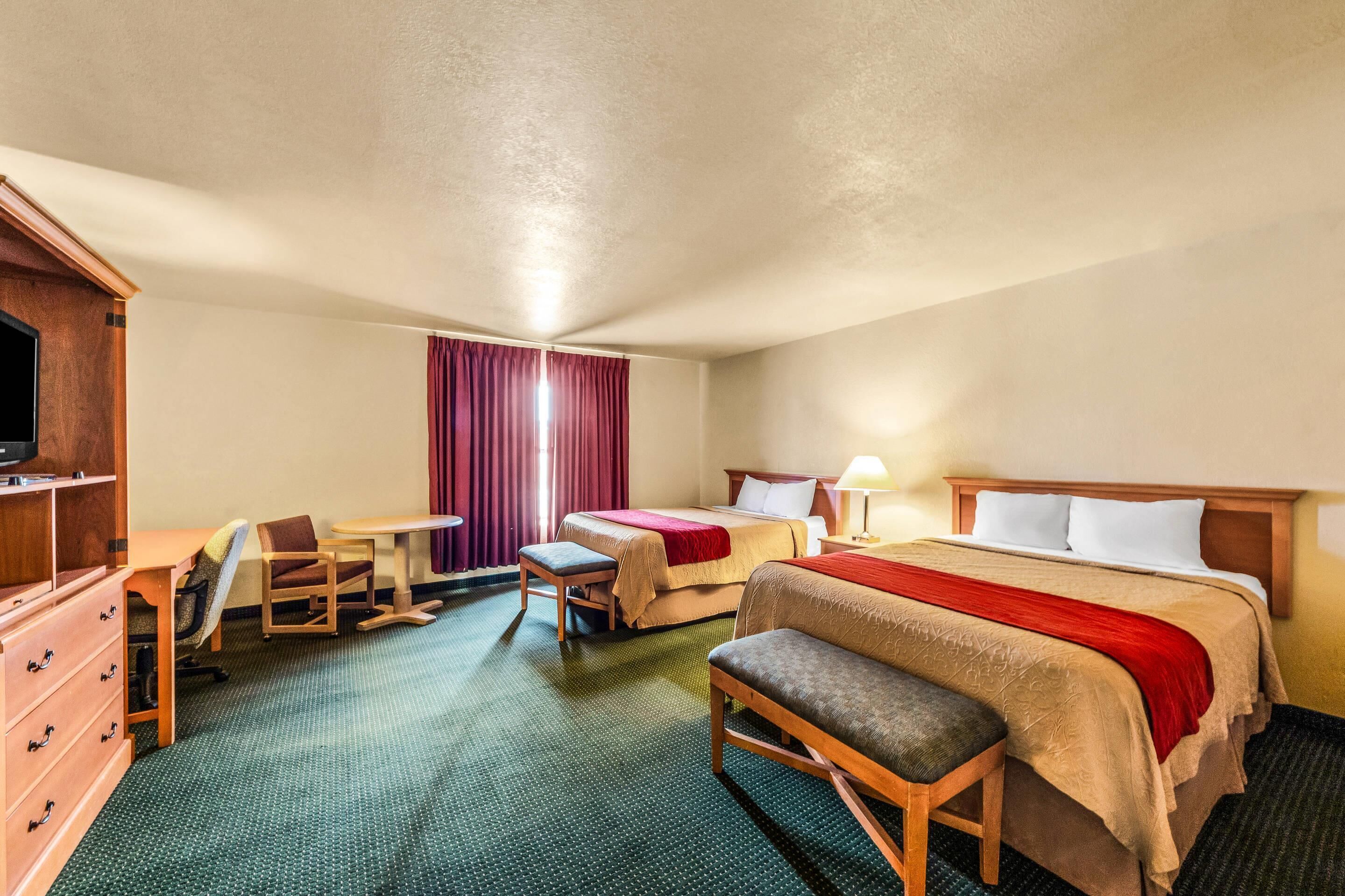 A hotel room with a bed, a desk, a chair, a TV, and a window with curtains.