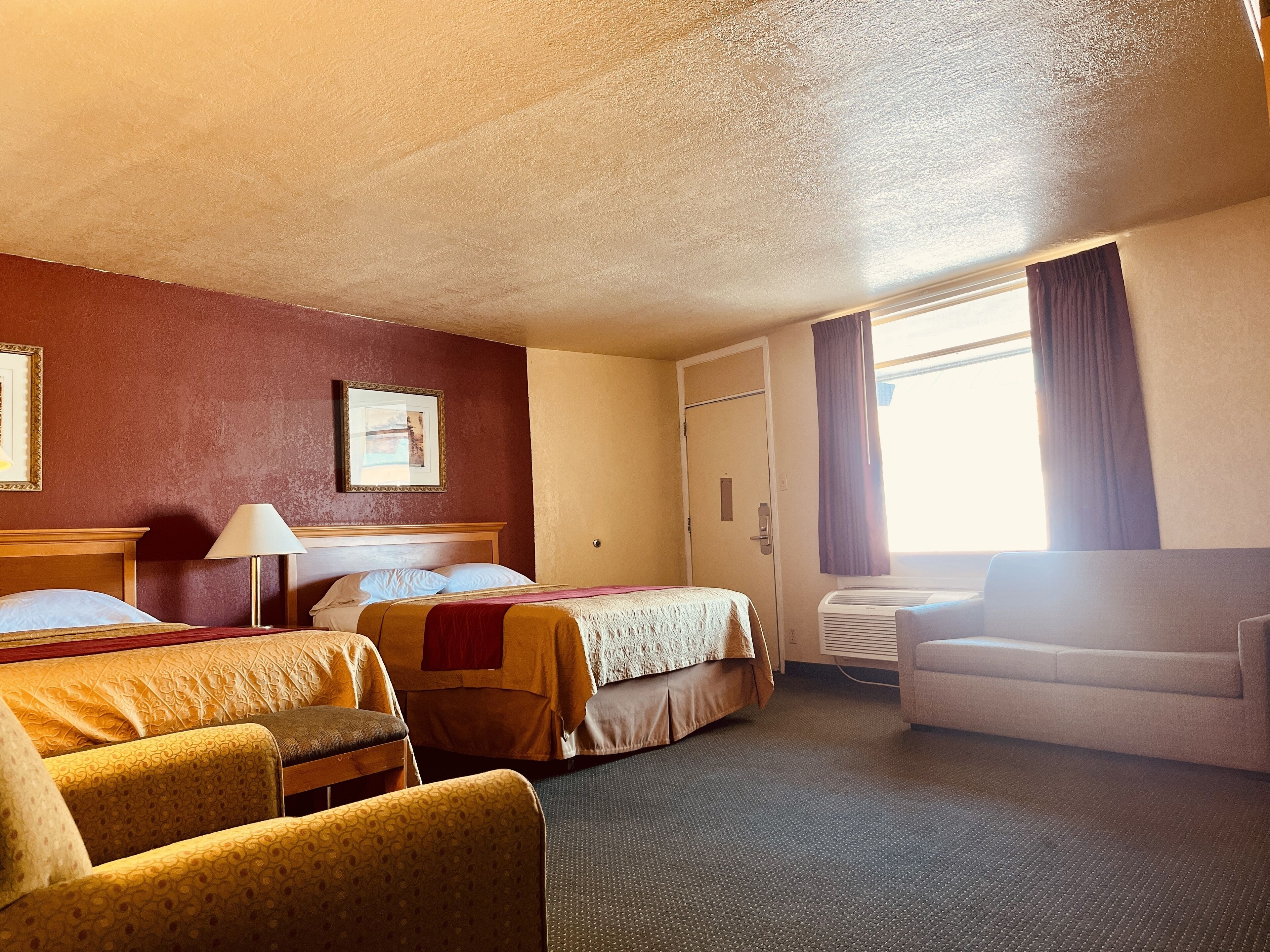 Une chambre d’hôtel avec deux lits, un canapé, une lampe et une fenêtre avec des rideaux.