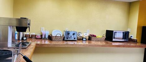 A coffee station with a coffee machine, microwave, and various food items.
