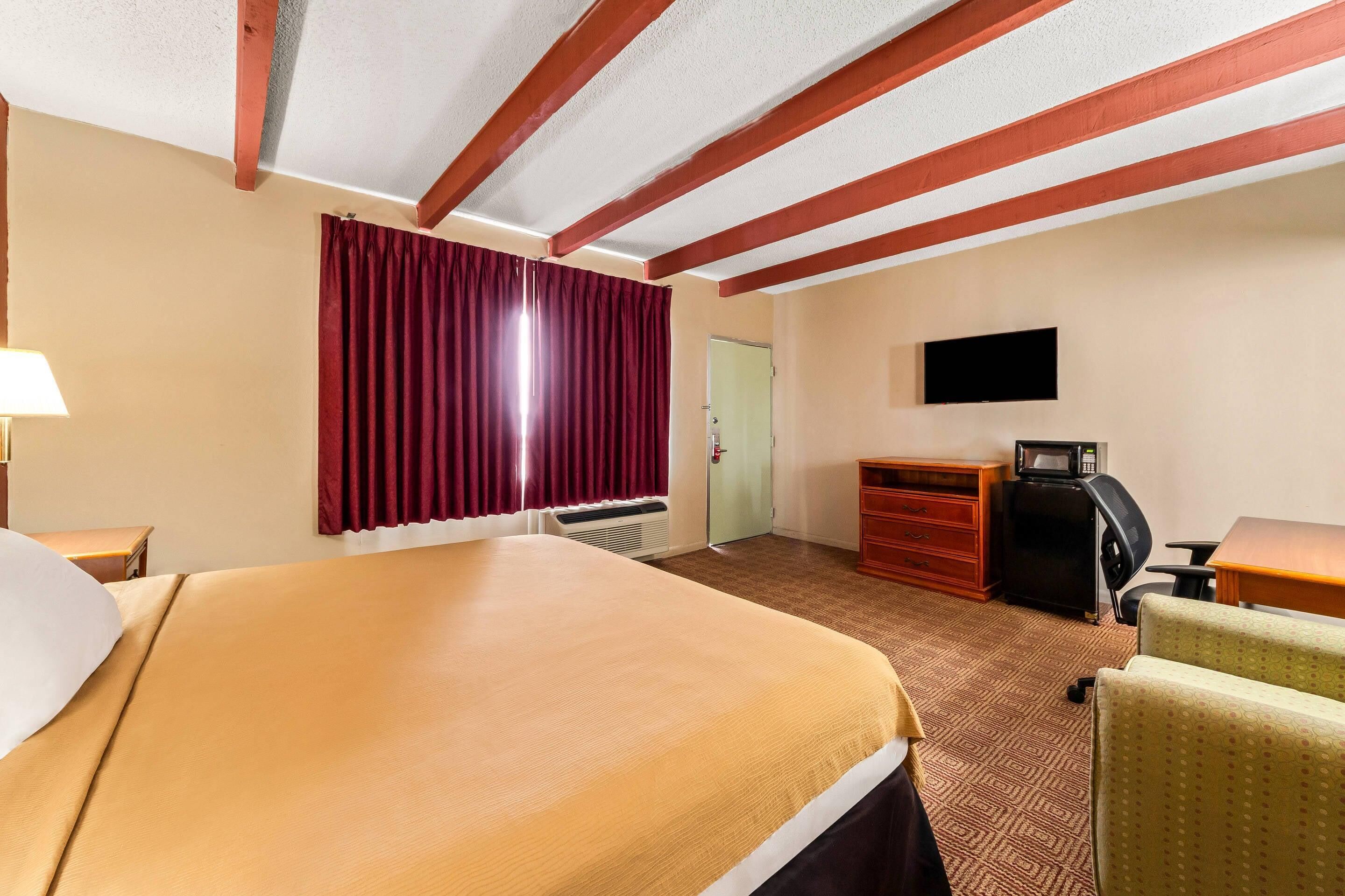 A hotel room with a large bed, a desk, a chair, a TV, and a wardrobe.