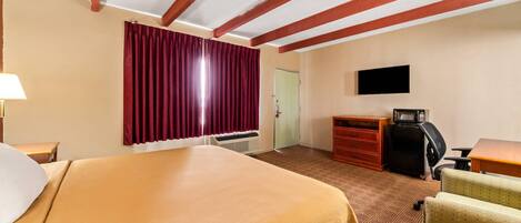 A hotel room with a large bed, a desk, a chair, a TV, and a wardrobe.