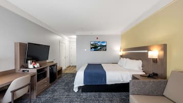 Habitación de hotel con cama, escritorio con televisor, sofá y televisor de pared.