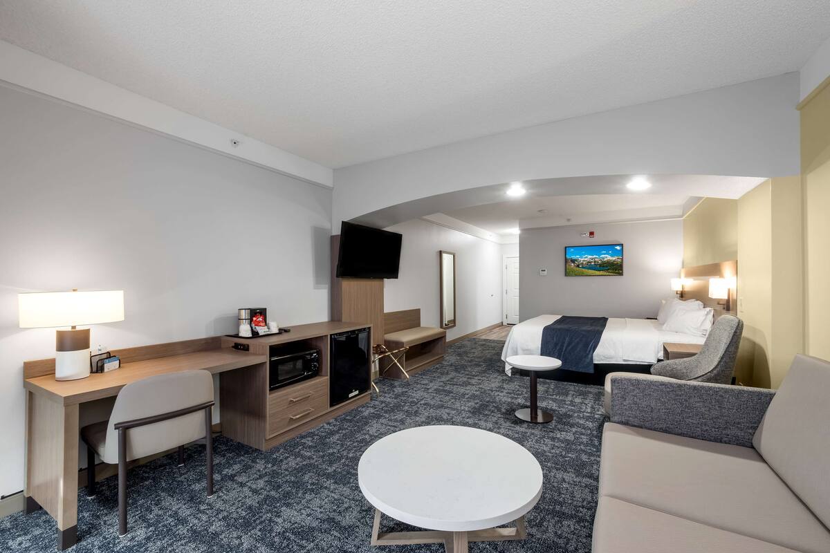 Une chambre d’hôtel équipée d’un bureau, d’une chaise, d’un lit, d’un canapé et d’une table ronde.