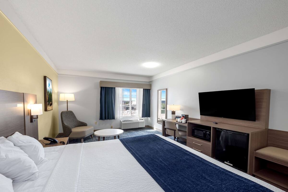 Une chambre d’hôtel dotée d’un grand lit, d’un téléviseur à écran plat, d’un bureau avec une chaise, d’une petite table et d’une cheminée.