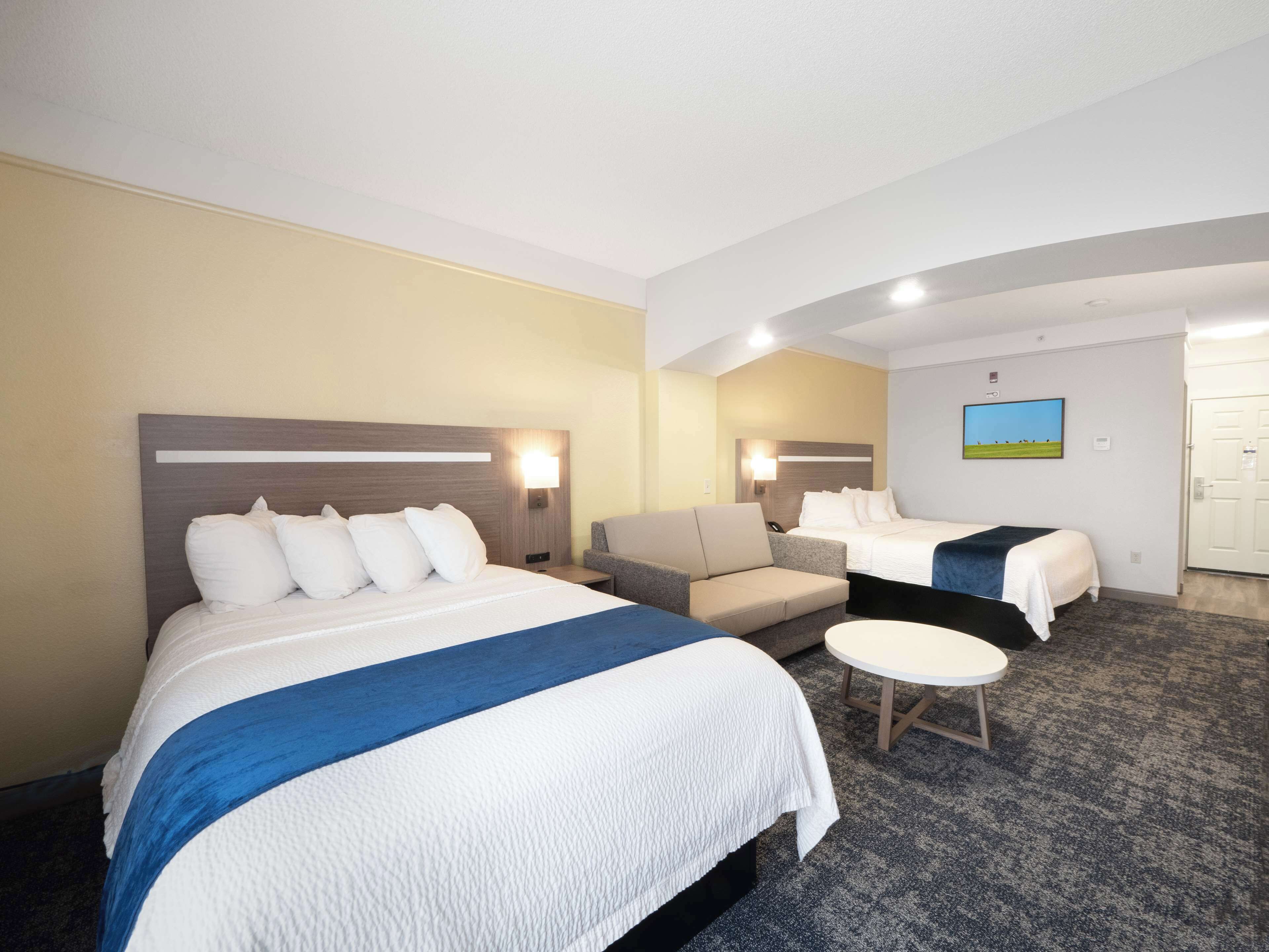 Une chambre d’hôtel avec deux lits, un canapé, une petite table et un tableau au mur.