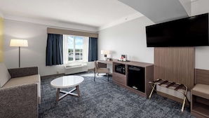 Une chambre d’hôtel équipée d’un téléviseur à écran plat, d’un canapé, d’une table à manger, d’un meuble pour la télévision avec un four à micro-ondes, et d’une fenêtre avec des rideaux.