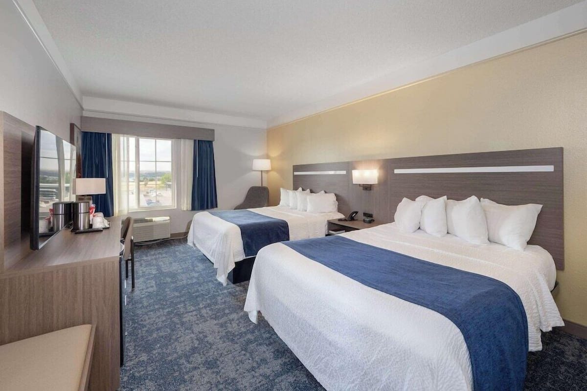 Une chambre d’hôtel avec deux lits, un bureau doté d’un téléviseur à écran plat, une chaise et une fenêtre avec des rideaux.