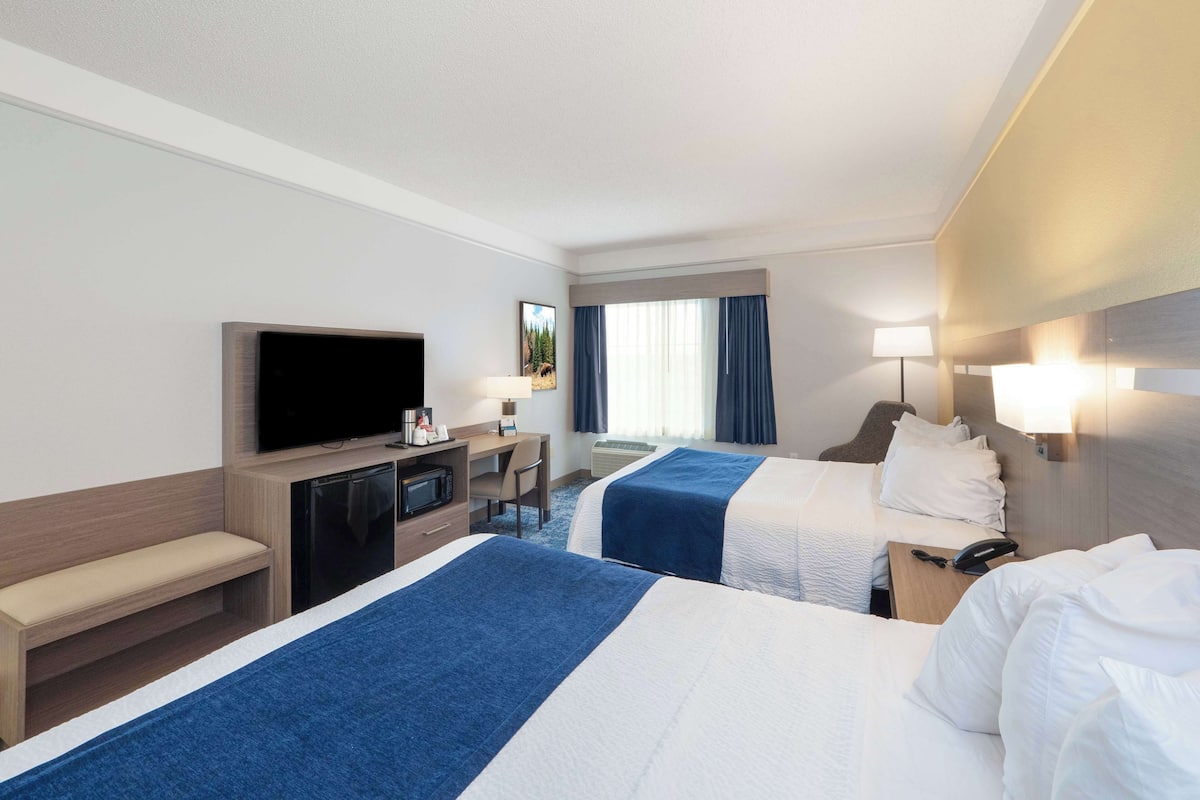 Une chambre d’hôtel avec deux lits, une télévision, un bureau avec un ordinateur et une fenêtre avec des rideaux.