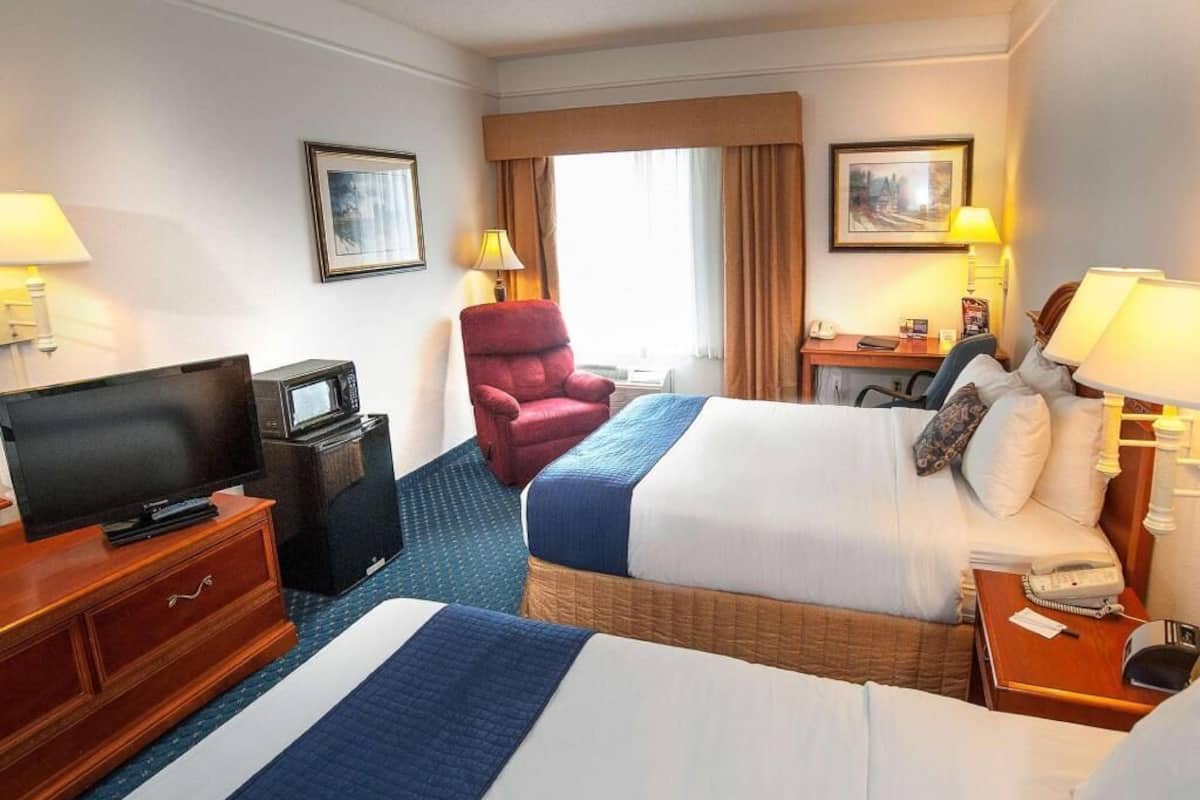 Une chambre d’hôtel avec deux lits, une télévision, un bureau avec une lampe et une chaise.