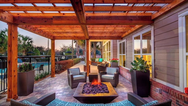 Un patio cubierto con una chimenea, mobiliario exterior y una piscina al fondo.