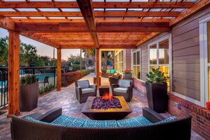 Une terrasse couverte avec un foyer, du mobilier d’extérieur et une piscine en arrière-plan.