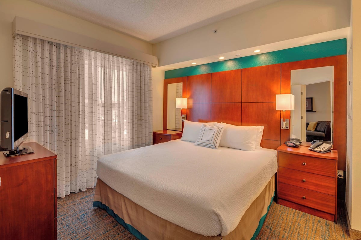 A hotel room with a large bed, a TV on a wooden cabinet, a desk with a lamp, and a mirror on the wall.