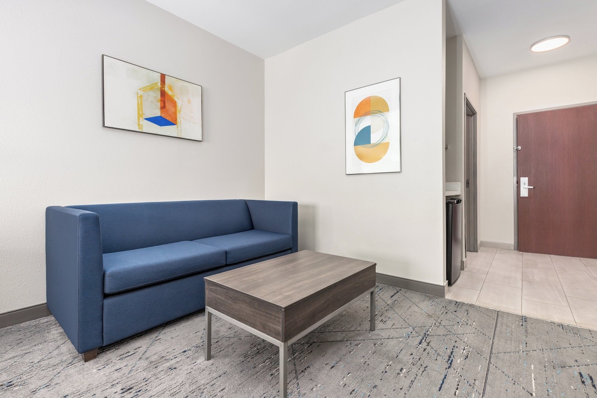 A modern hotel lobby with a blue sofa, a wooden coffee table, and two abstract paintings on the walls.