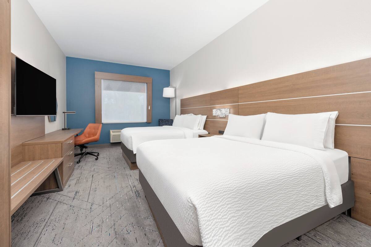 A hotel room with a large bed, a desk, a chair, a TV, and a window.
