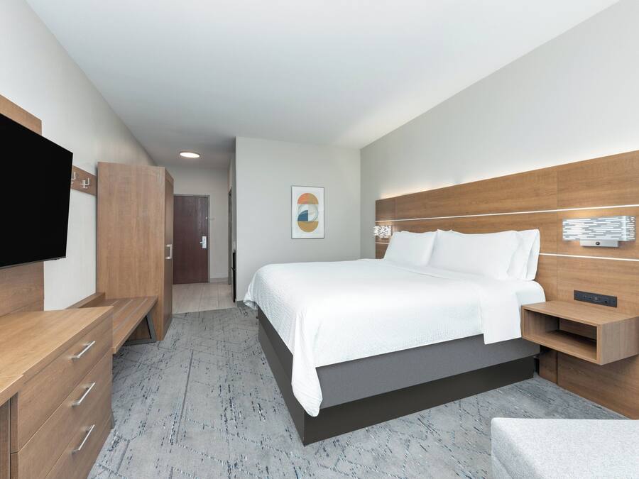 Ein modernes Hotelzimmer mit einem großen Bett, Holzmöbeln, einem Flachbildfernseher und einer wandmontierten Leuchte.