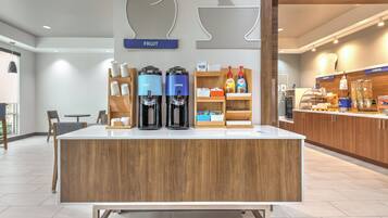 A coffee station with two coffee makers, a fruit display, and a cereal section in a modern cafe setting.