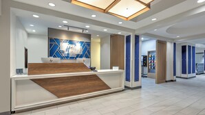 Een moderne receptie met een houten receptiebalie, een blauw geometrisch wandontwerp en een plafond met inbouwverlichting.