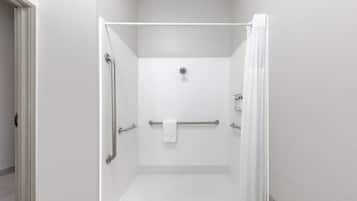 A white, enclosed shower area with a glass door, a towel rack, and a handrail.