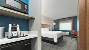 Een hotelkamer met een bed, een bureau met een koffieapparaat, een magnetron en een raam.