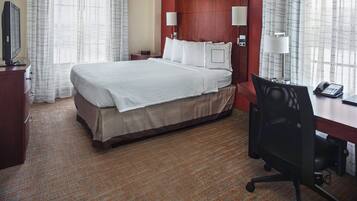 Una habitación de hotel con una cama grande, un escritorio con silla, un televisor y dos lámparas.