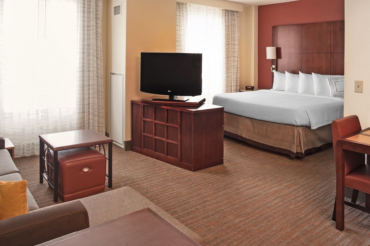 Quarto de hotel com uma cama, televisão, escrivaninha, cadeira e sofá.