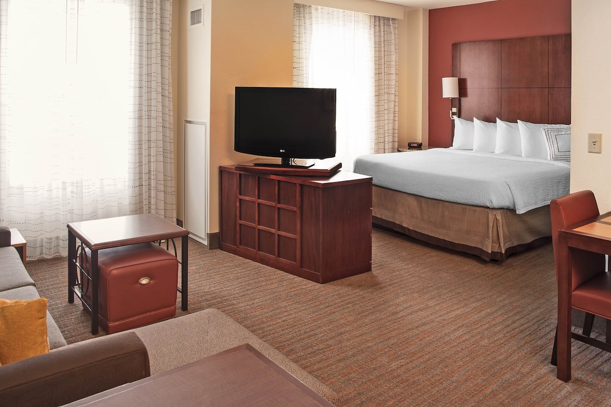 Quarto de hotel com uma cama, uma televisão sobre um suporte de madeira, uma escrivaninha e uma cadeira.