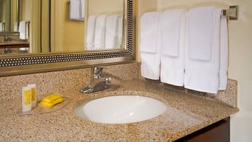 Un bagno con piano di lavoro in granito, lavandino bianco, specchio con cornice decorativa e due asciugamani bianchi su un portascopevoli.