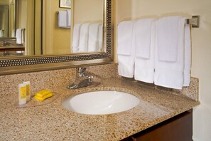 A bathroom with a granite countertop, a white sink, a mirror with a decorative frame, and two white towels hanging on a towel rack.