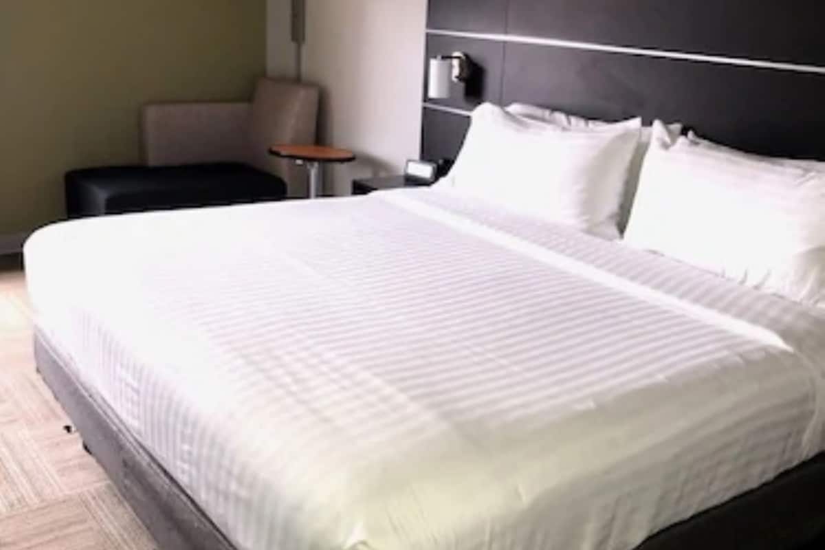 A hotel room with a large bed, a bedside table, a chair, and a lamp.