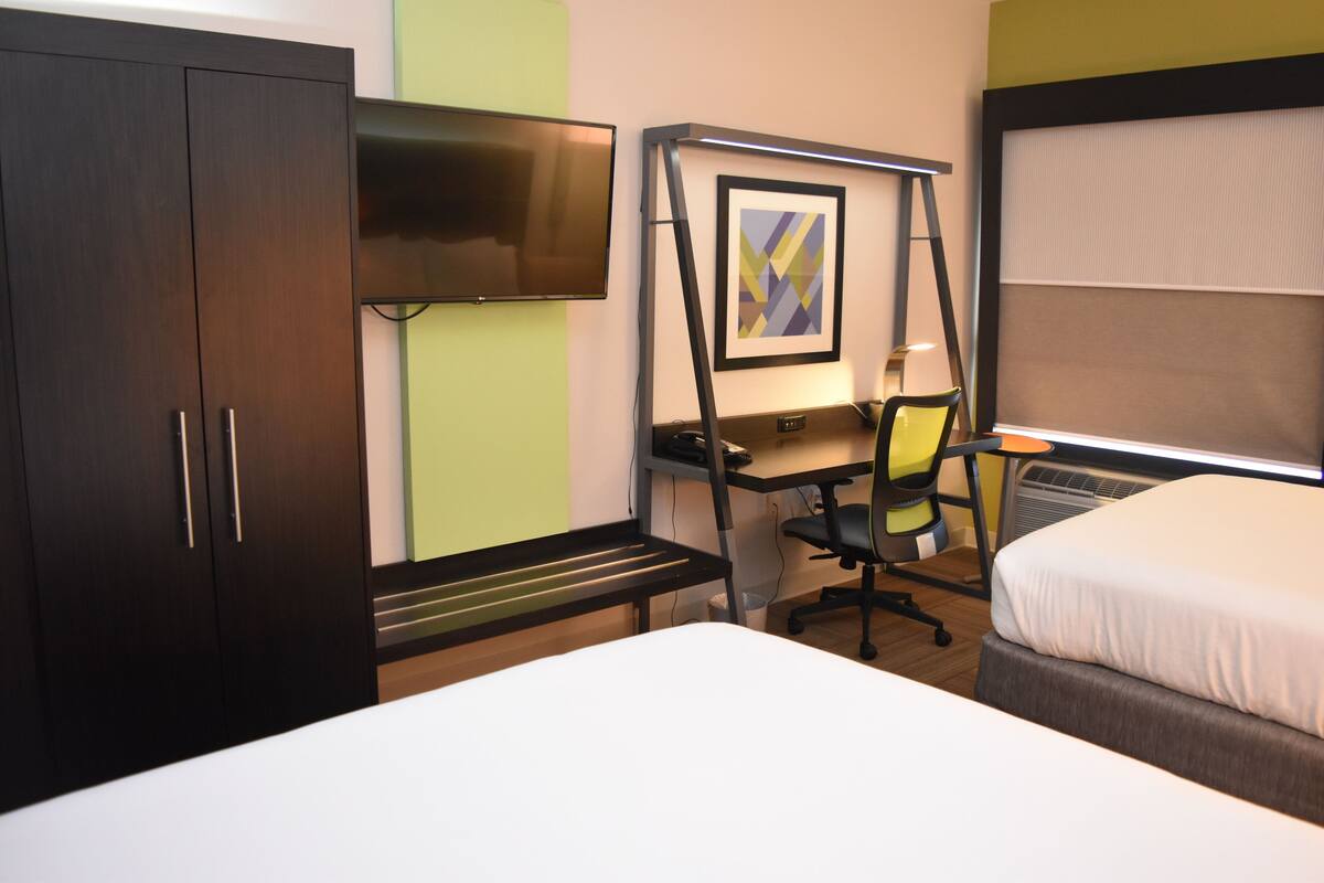 A hotel room with a bed, a desk with a chair, a TV, and a framed picture on the wall.