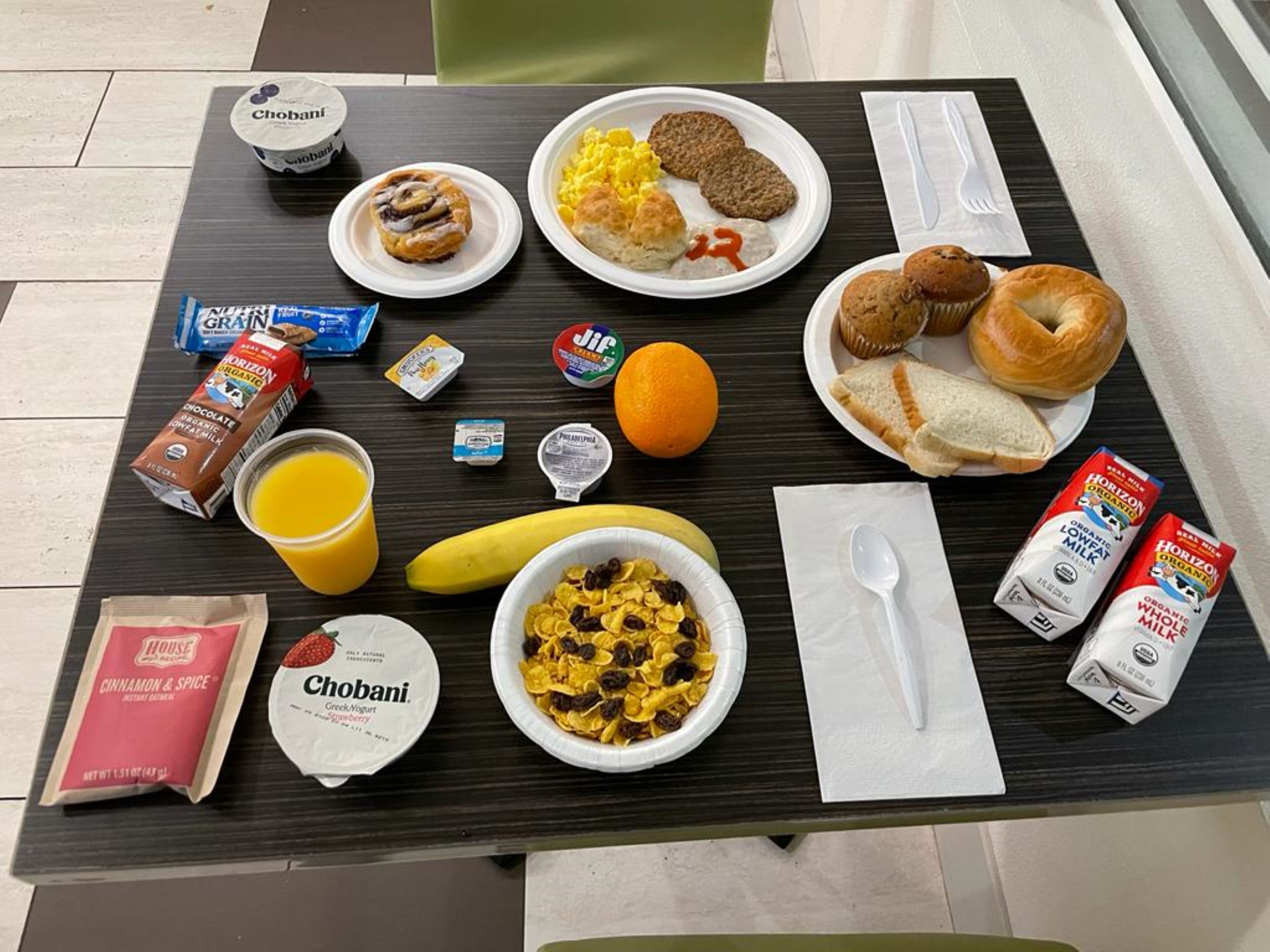 Una mesa de desayuno con diversos alimentos y bebidas, incluyendo yogur Chobani, leche orgánica Horizon y un plátano.