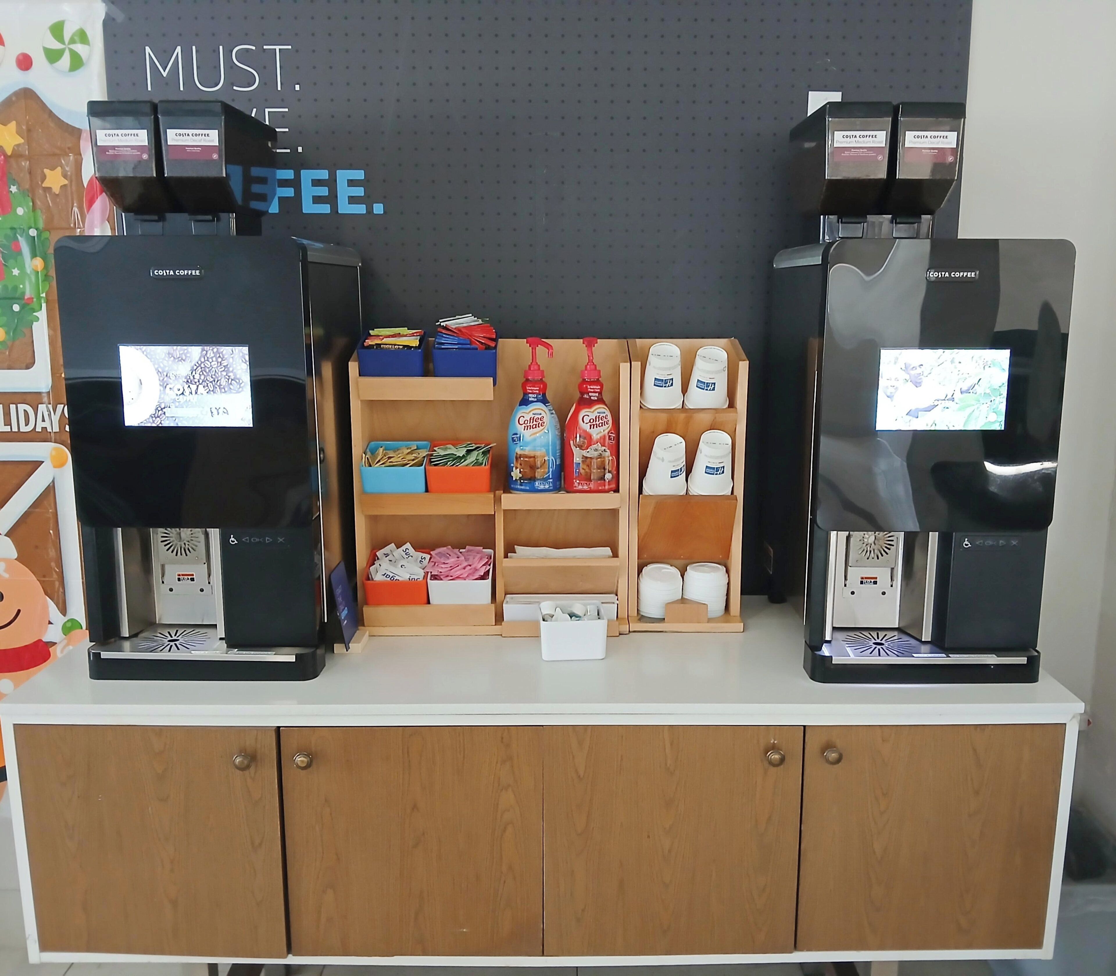 Una estación de café con dos máquinas de café, un estante con cápsulas de café y una exhibición de tazas de café.