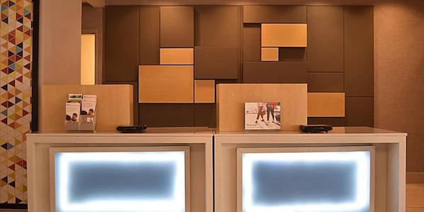 A reception desk with a modern design, featuring a geometric wall pattern and a neutral color scheme.