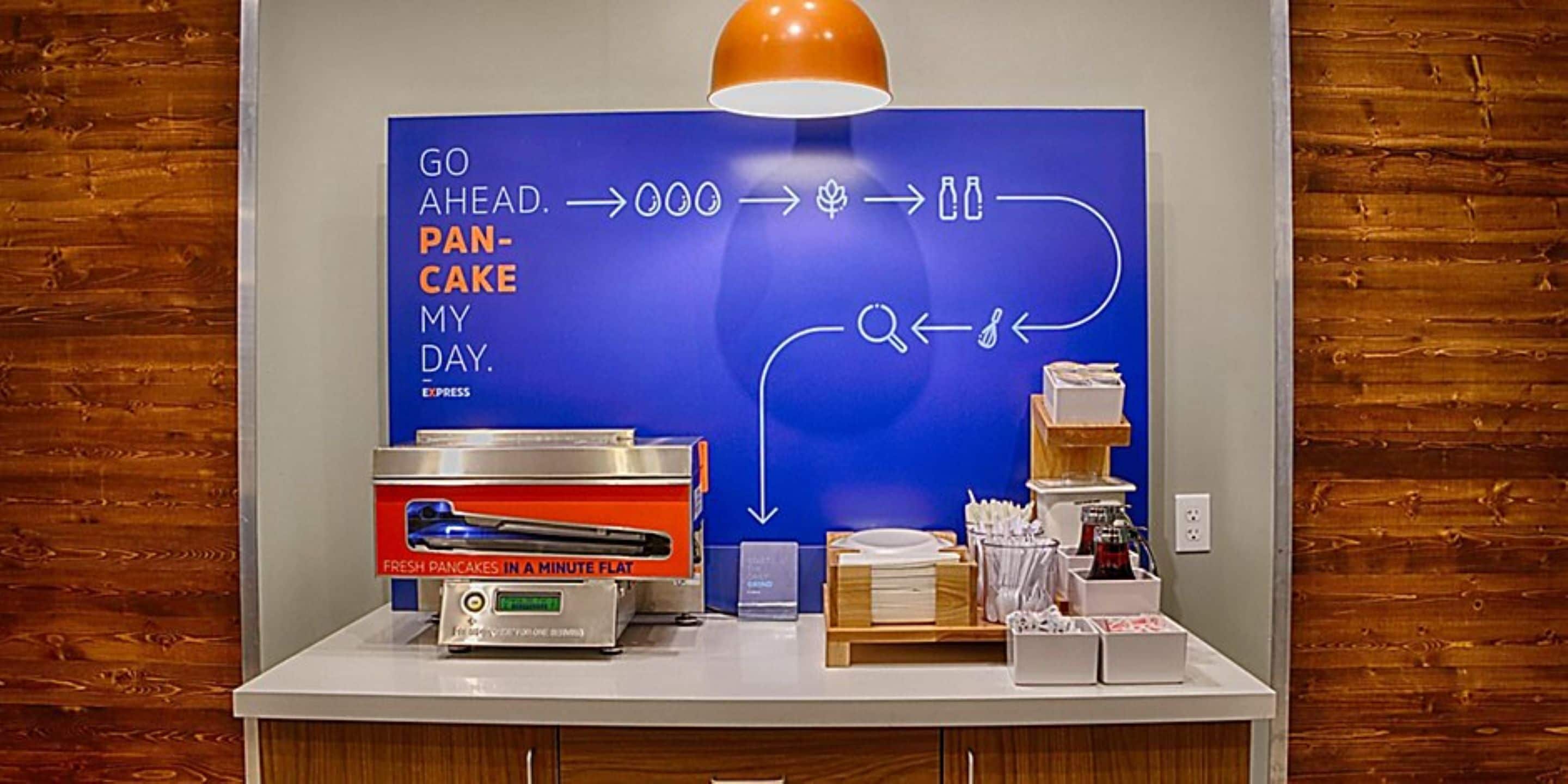 A breakfast station with a blue sign, a pancake maker, and breakfast items.