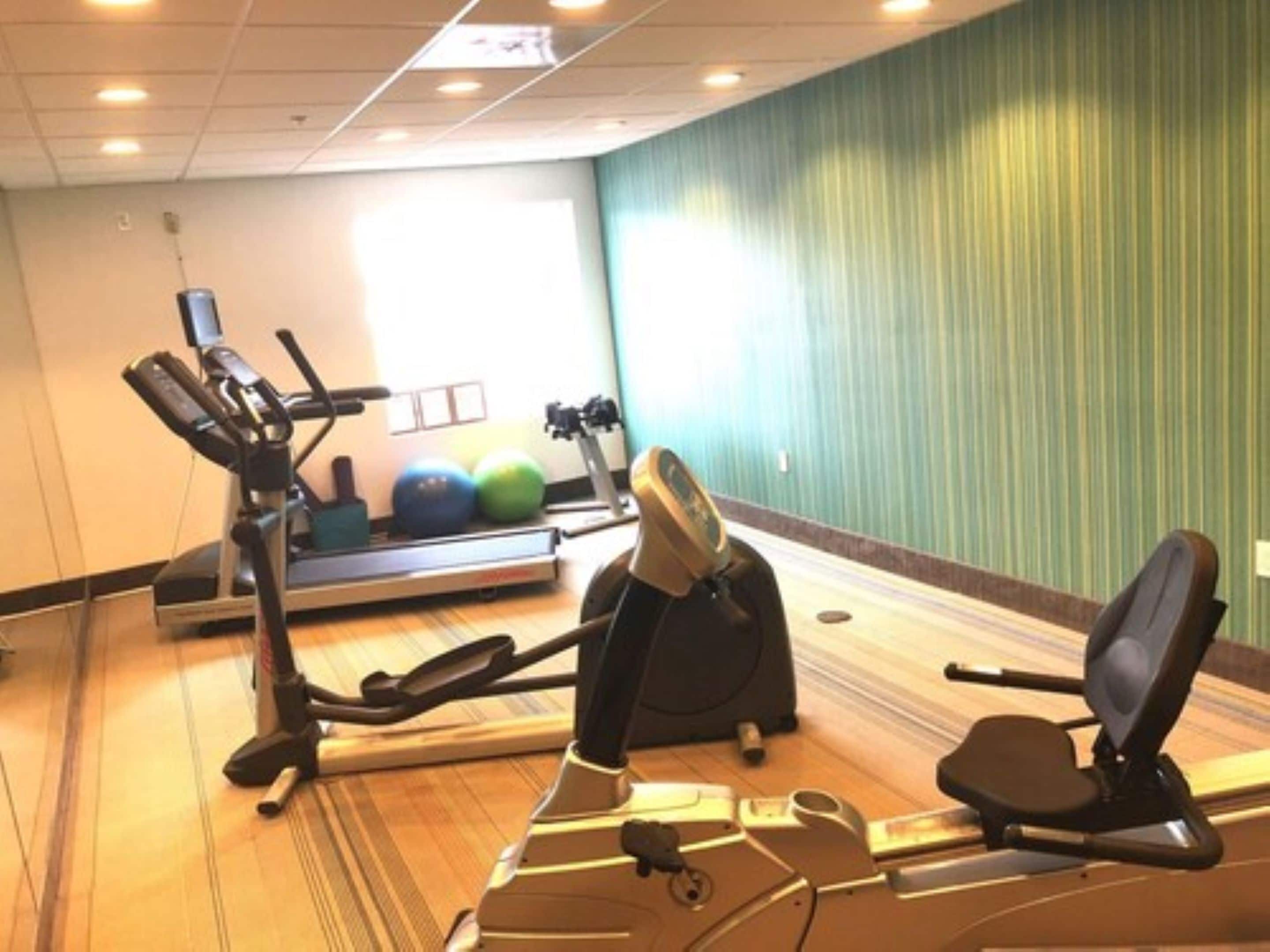 A gym with exercise equipment including treadmills, stationary bikes, and exercise balls.